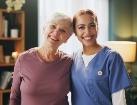 a caregiver standing beside an elderly woman, both smiling