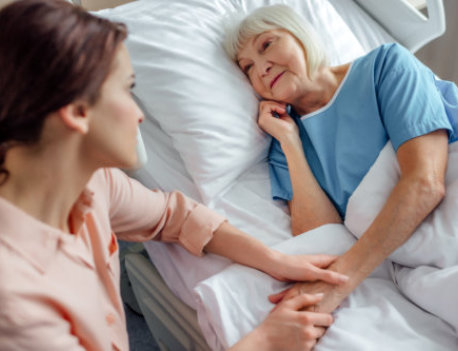 a caregiver gently holding the hand of an elderly woman resting in a hospital bed
