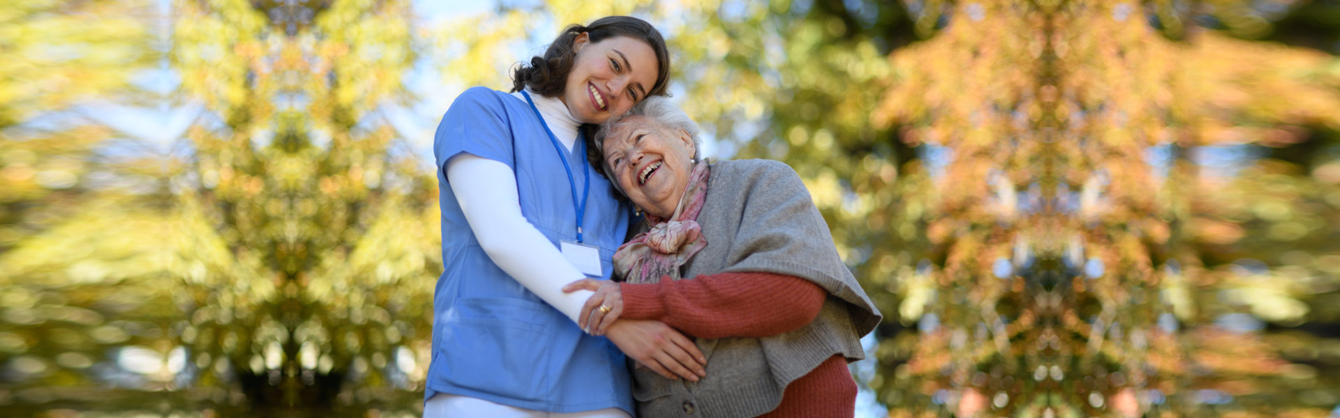 Portrait of nurse and elderly woman on walk in the park during warm autumn day