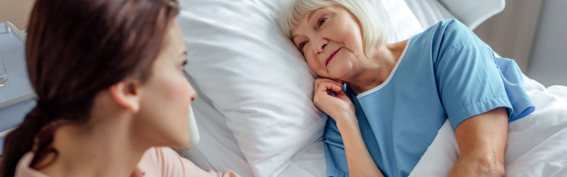 daughter sitting near elder mother in bed and holding hands in hospital